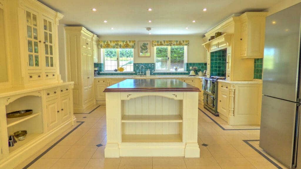 Spacious, bright kitchen with cream cabinets, a wooden-topped island, green tiled backsplash, stainless steel refrigerator, and large windows—perfect for Airbnb Management or Holiday Home Cleaning services.